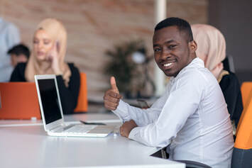 Black man at a computer desk giving a thumbs up
