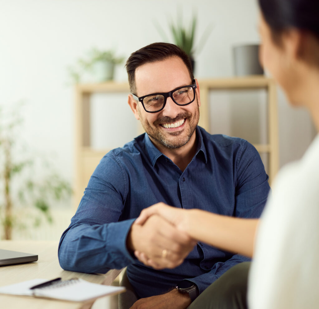 Positive handshake between professionals in an office environment with a smiling demeanor.